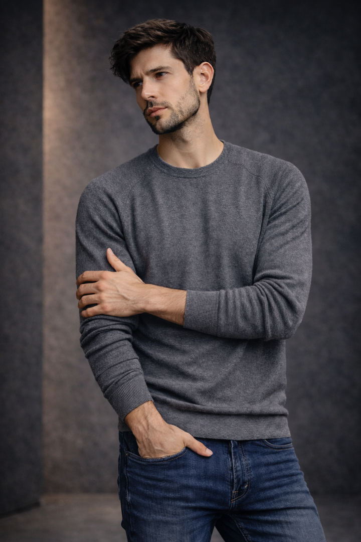 Man wearing a gray sweater and blue jeans against a dark background